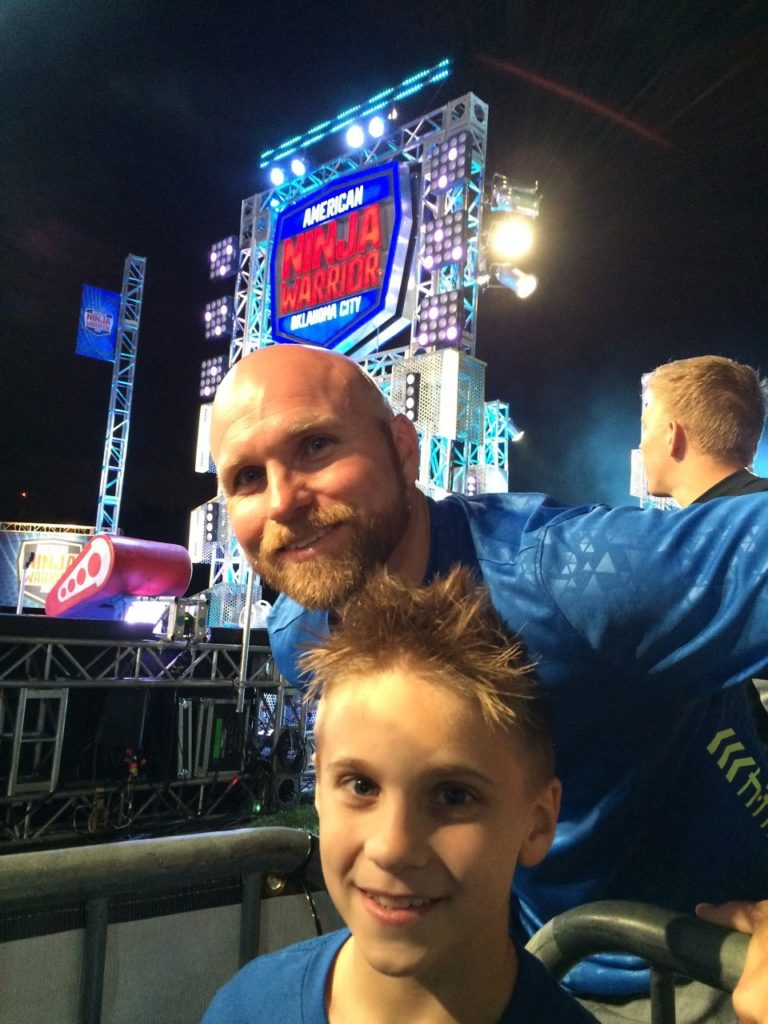 Grant Clinton with his son posing in front of ANW sign