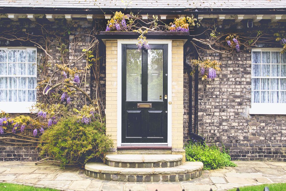 photograph of front door to a home with wysteria vines and purple flowers in front of brick facade