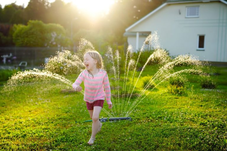 Young-girl-running-through-lawn-sprinkler - Benchmark